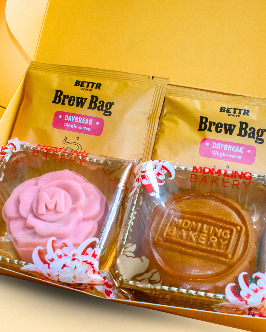 A gift box set featuring two packets of BETTR Coffee's Daybreak Brew Bag and two packaged mooncakes from Mdm Ling Bakery: a pink rose-shaped mooncake and a round traditional baked mooncake.